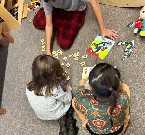 Young native children playing on the floor together with letters and a Haida whale puzzle