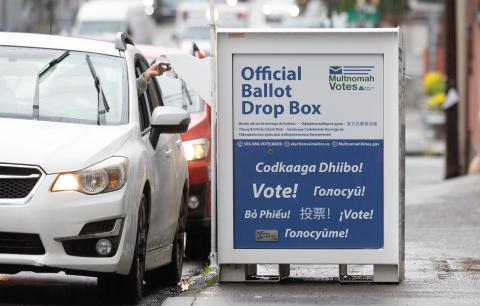 voter inside of vehicle drops off ballot at drive up official ballot drop box 