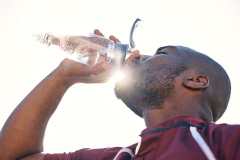 Man drinking a glass of water as the sun shines behind the glass