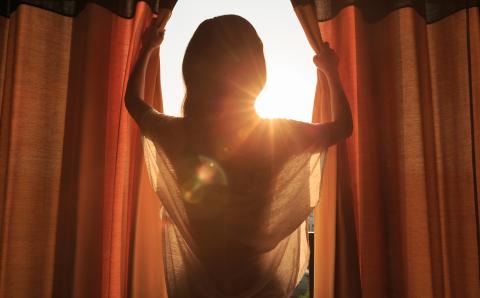 Person closes dark colored curtains while the sun shines into the room