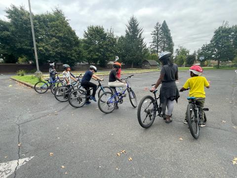 Five kids with bikes paying attention to an adult standing next to her own bike.