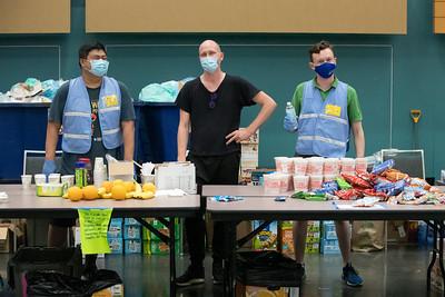 three people with brightly color vests on stand behind a table with supplies for visitors to a cooling center