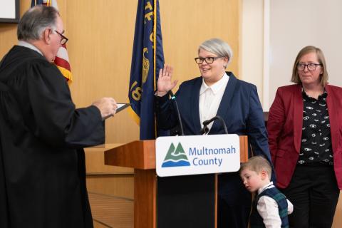 Commissioner Moyer receiving the Oath of Office with her son at her side and wife standing behind her.