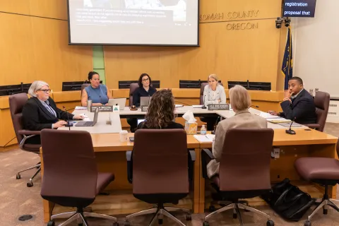 Multnomah County Commissioners are sitting around a table together with staff, discussing the budget.