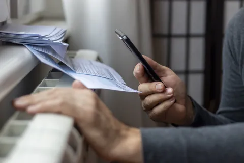 Resident standing by heater and checking utility bill while picking up the phone