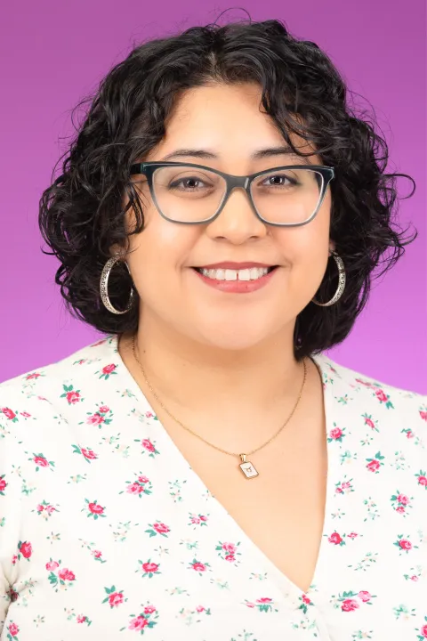 Beatriz smiling in a floral top with a pink background