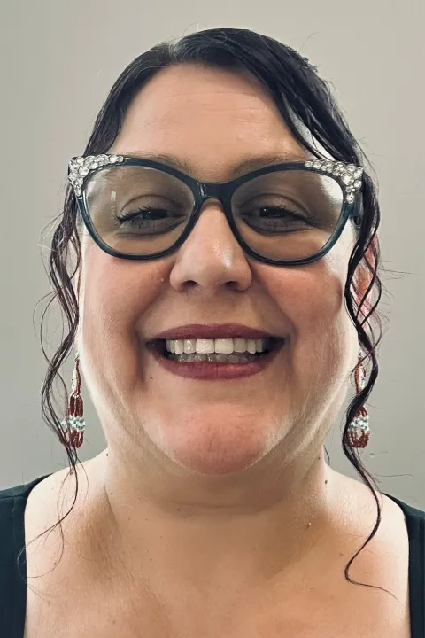 Brandi smiling with glasses on, a black top and grey background