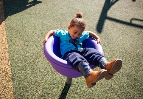 young child in a swing with a big smile as the sun is shining