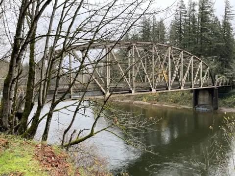 Stark Street bridge over the Sandy River, with bare trees in the foreground and evergreens on the further bank