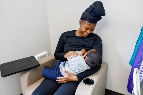 A Black woman breastfeeding a child in a lactation room and smiling