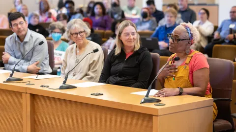 Cuatro miembros de la comunidad testifican en una audiencia pública sobre el presupuesto en la sala de juntas del condado.