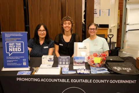 Three people at a table with ombudsperson information.