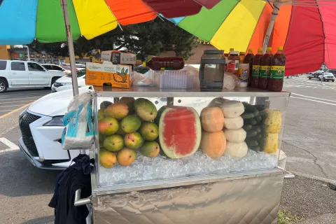 Rainbow umbrellas shade a tropical fruit stand.