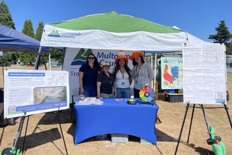 Four people stand smiling behind an information table at an outdoor event.