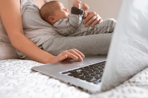 Người mẹ bế em bé trong khi sử dụng máy tính xách tay.